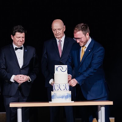 Skupina čtyř mužů v oblecích slaví s dortem na pódiu, symbolizující úspěch a týmovou spolupráci v rámci Kometa Family.