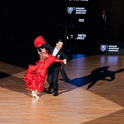 Taneční pár Kometa Family předvádí latinskoamerický tanec na soutěžním parketu, v elegantním oblečení, s dynamickým pohybem a výraznou choreografií.